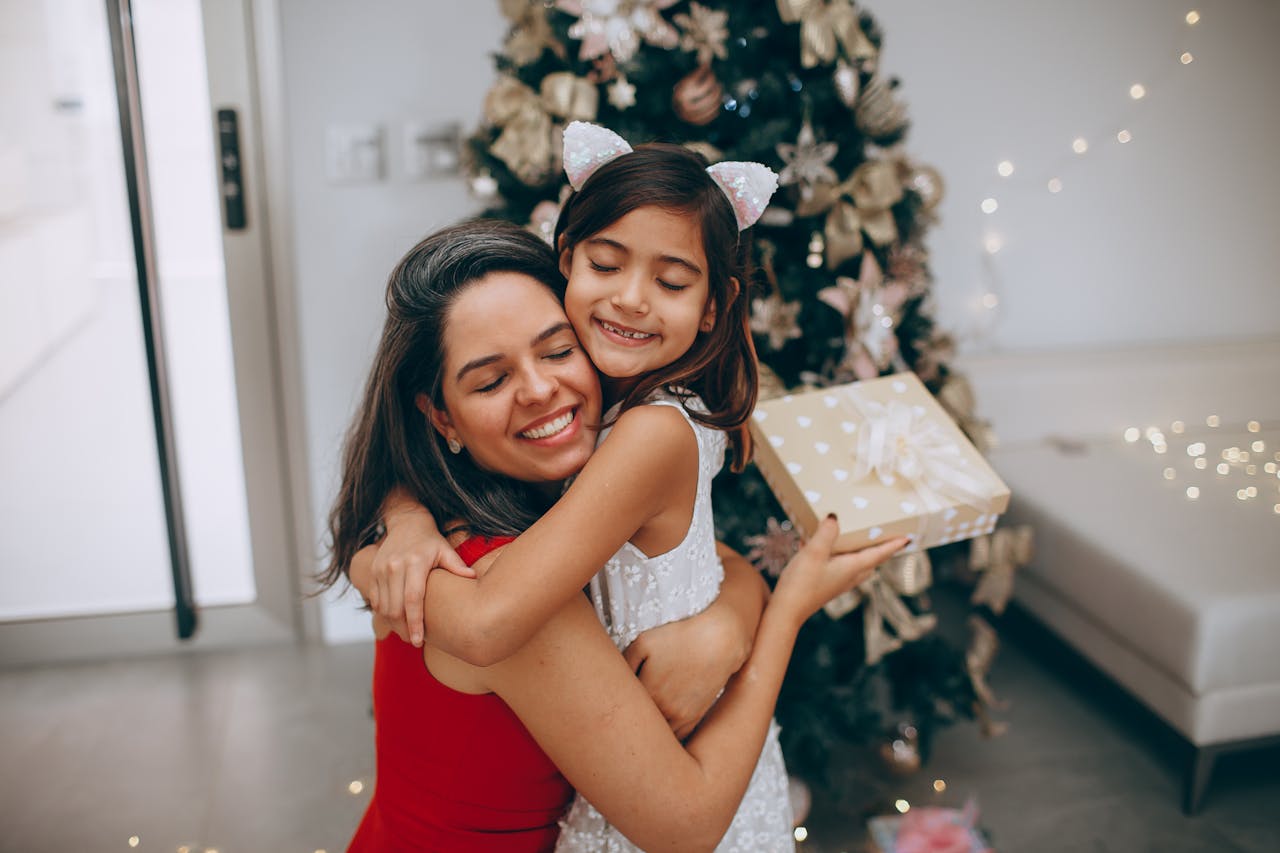 A Woman and a Girl in a Hug Against a Christmas Tree